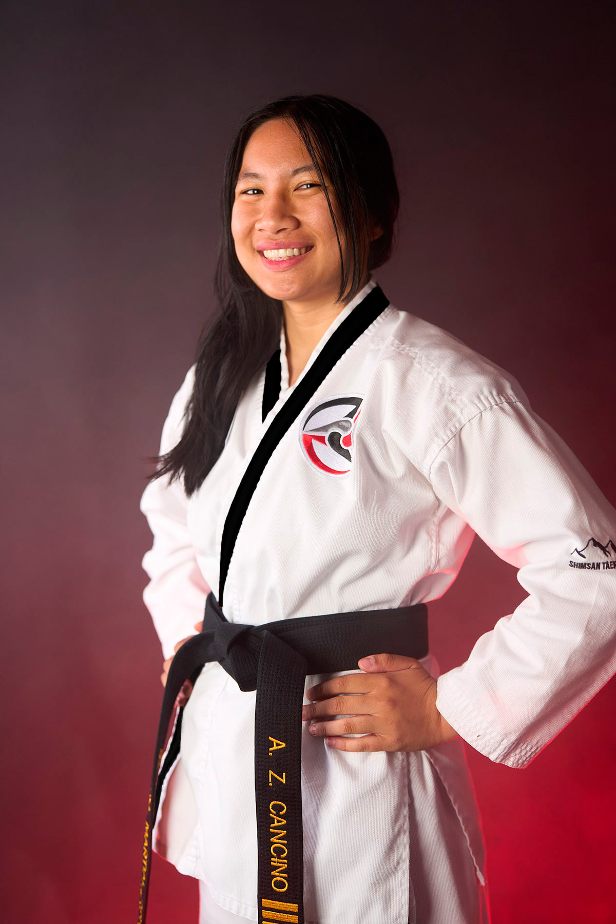 Ms. Alysha Cancino poses with her hands on her hips in a white taekwondo uniform, wearing a black belt